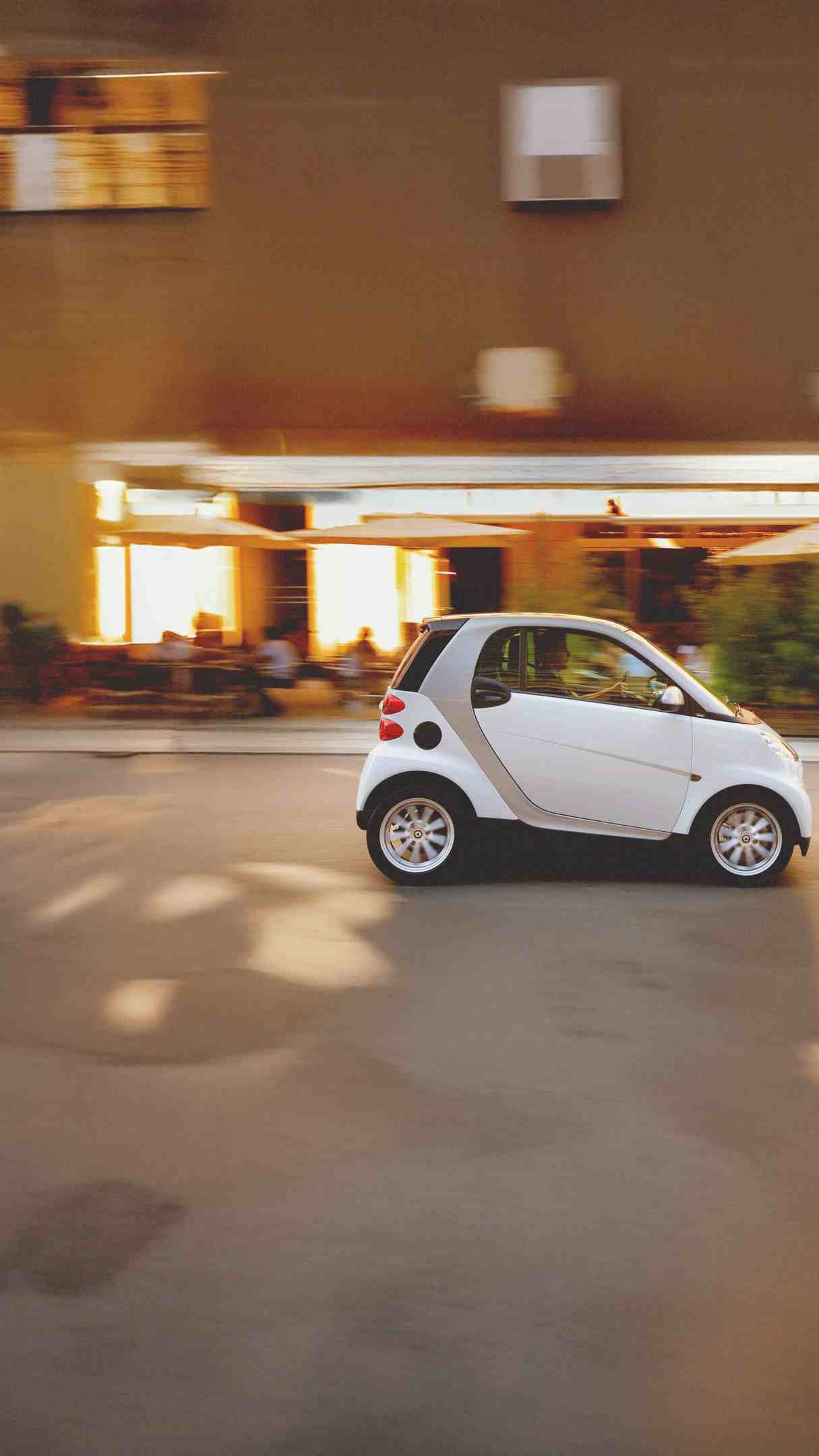 Ein weißer smart fortwo fährt an einem Café vorbei.